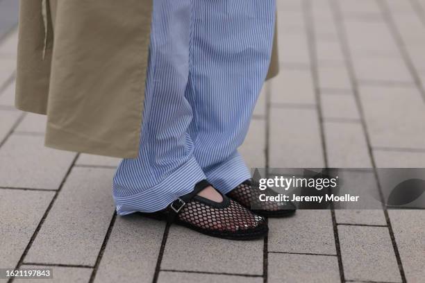 Maria Barteczko seen wearing Arket blue button down shirt, blue striped pajamas pants, NA-KD beige oversized long trenchcoat, Source Unknown black...