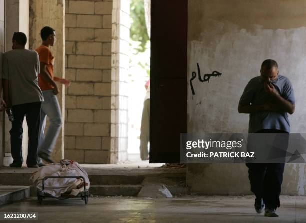 Lebanese man covers his nose and holds his stomach as he walks past a corpse 09 August 2006 awaiting identification at a religious morgue in Beirut...