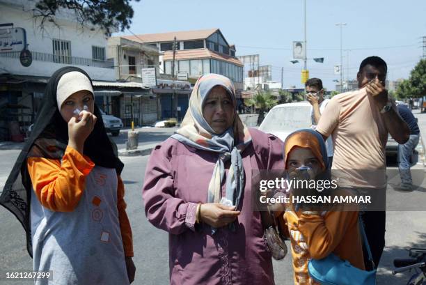 Lebanese civilians cover their noses and mouths from the stench of dead bodies being put in coffins by the Lebanese army, in an open air parking lot...