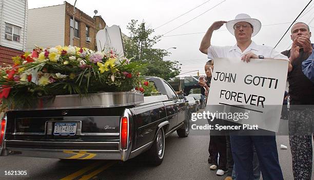 An admirer of legendary crime boss John Gotti salutes and holds a sign which reads," John Gotti Forever" as Gotti's funeral procession passes by the...