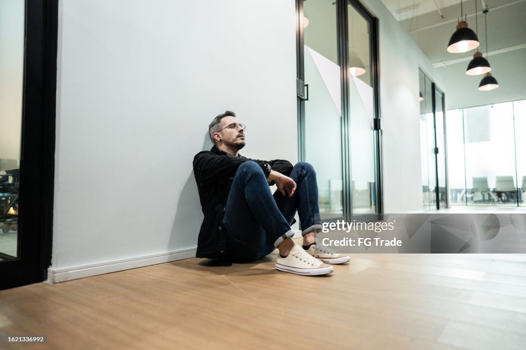 Worried businessman sitting on ground at office corridor