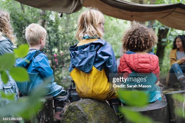 children sit round the campfire with their parents at forest school - bambini seduti in cerchio foto e immagini stock