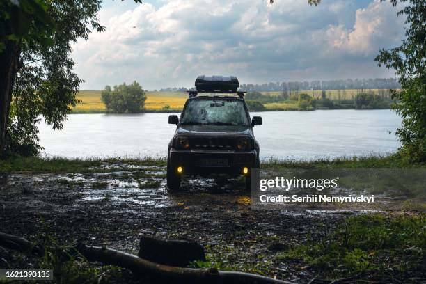 khmelnytskyi, ukraine - july 2, 2023: old suzuki jimny 2010 jb43 with black roof rack box on the top, outdoor, traveling by car. rainy summer day on the shore of the lake, forest. - car roof box stock-fotos und bilder