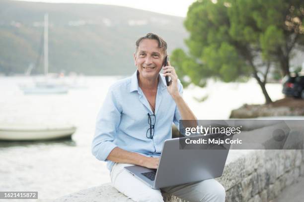 freelancer consulting using phone and laptop on beach - expatriate stock pictures, royalty-free photos & images