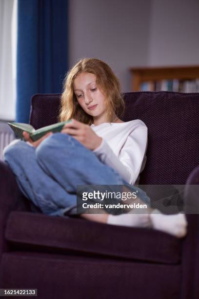 girl with red blonde hair reading a book - curled up reading book stock pictures, royalty-free photos & images