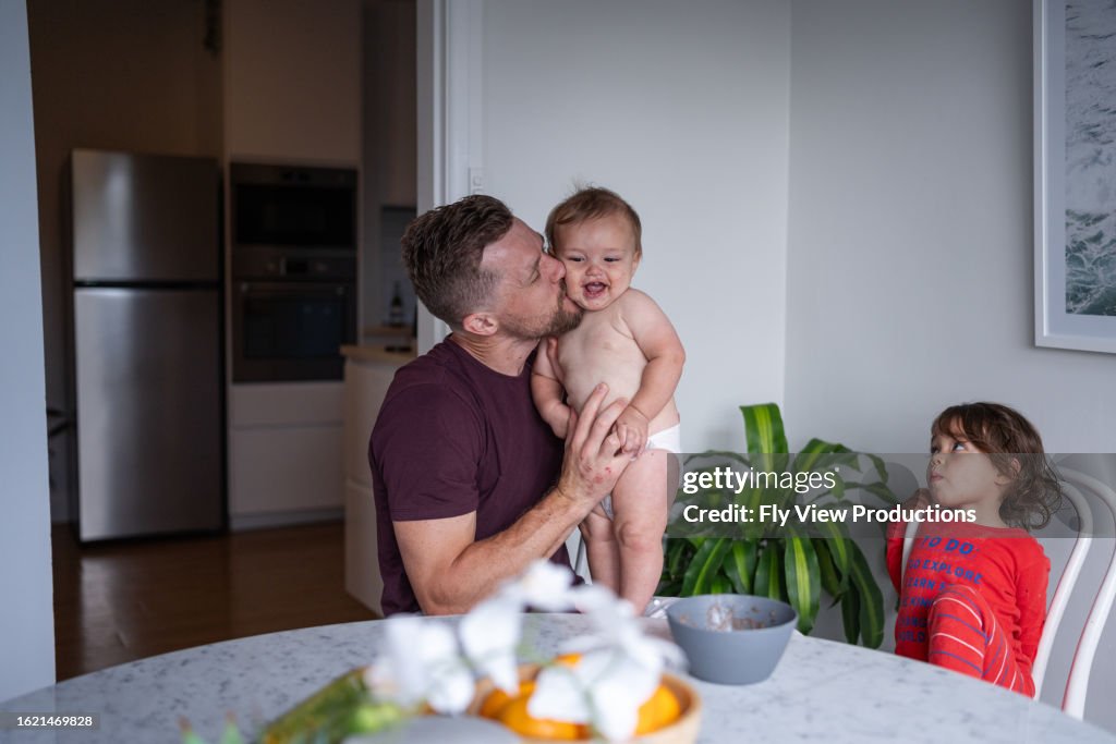 Father kisses son on cheek as daughter sits alongside the dining table