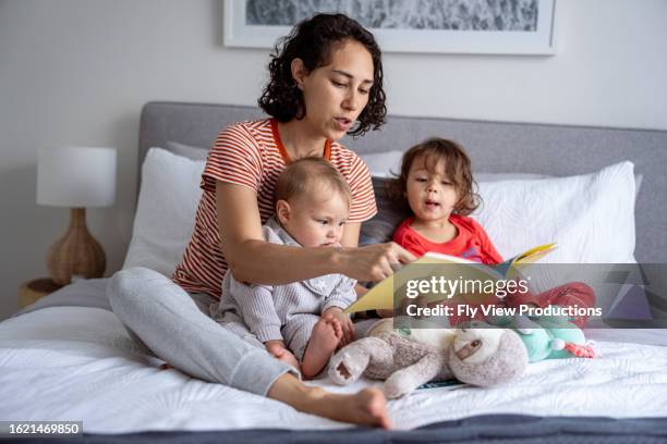 mother and two young children reading in bed - parents baby sister stock pictures, royalty-free photos & images