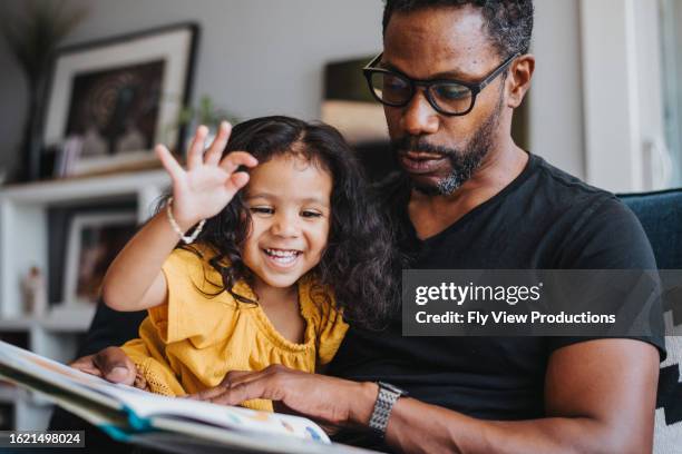 loving father reads a book with his mixed race daughter - modern manhood stock pictures, royalty-free photos & images