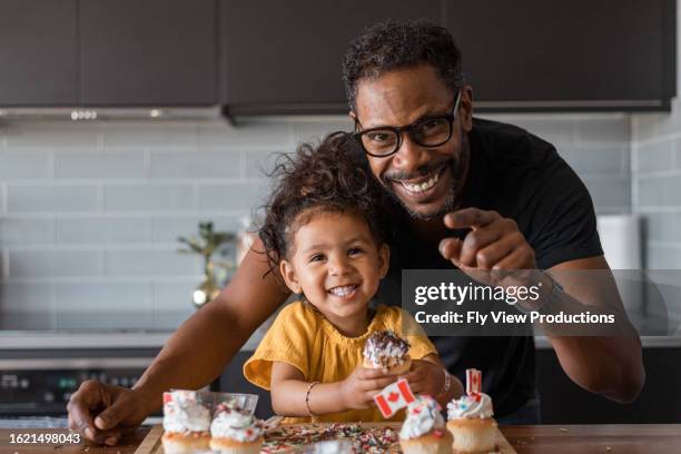father and young daughter decorate cupcakes at home - canada day stock pictures, royalty-free photos & images