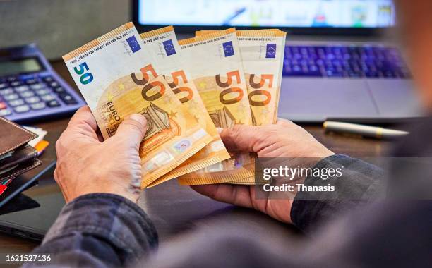 close-up of man's hand holding and counting money, - 50 euro stock pictures, royalty-free photos & images