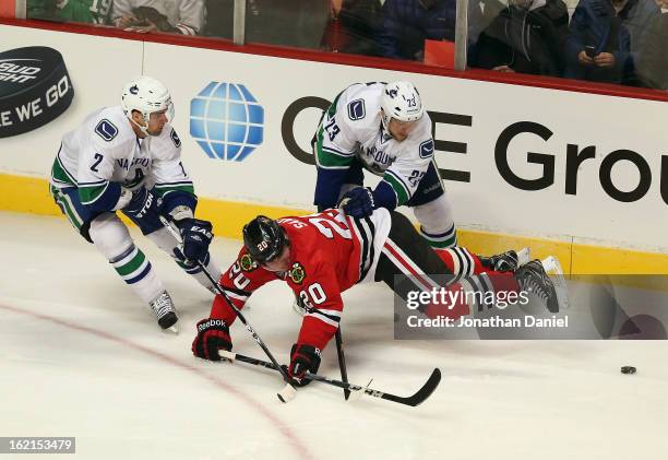 Brandon Saad of the Chicago Blackhawks is knocked to the ice by Alexander Edler and Dan Hamhuis of the Vancouver Canucks at the United Center on...