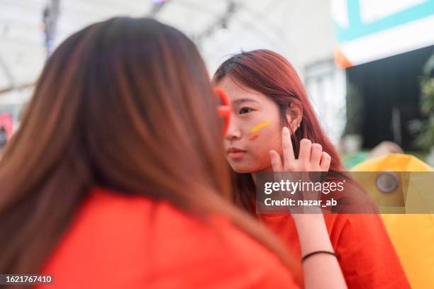 soccer fan putting face paint on getting ready for game. - football body paint stock pictures, royalty-free photos & images