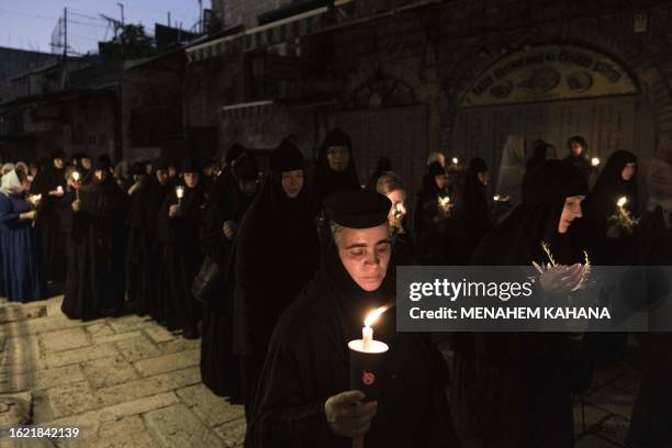 Orthodox nuns hold candles and flowers as they walk along the narrow streets of Jerusalem's Old City in a religious procession marking The Dormition...