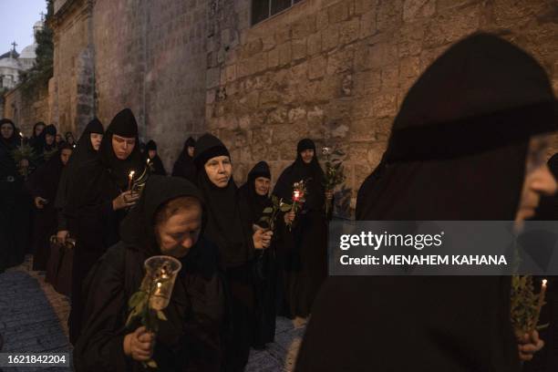 Orthodox nuns hold candles and flowers as they walk along the narrow streets of Jerusalem's Old City in a religious procession marking The Dormition...