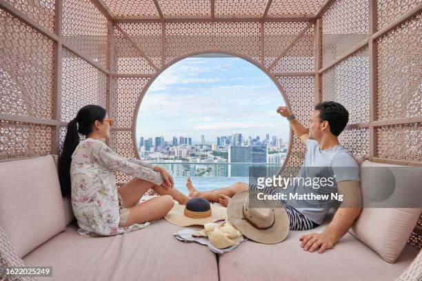 asian couple relaxing in a cabana by the hotel pool - the weekend in news around the world imagens e fotografias de stock