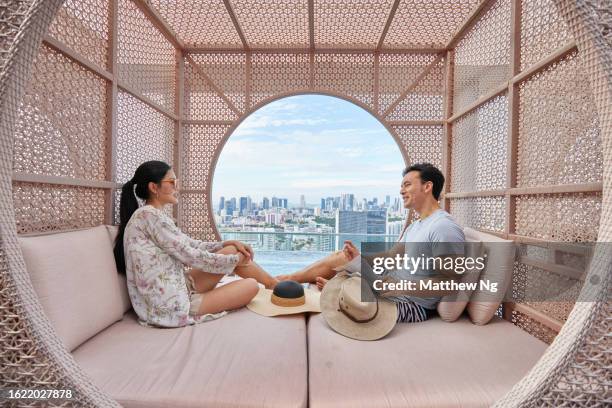 asian couple relaxing and laughing in a cabana by the hotel pool - luxury lifestyle stock pictures, royalty-free photos & images