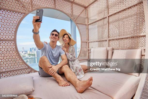 asiatisches paar, das ein selfie in einer cabana am hotelpool macht - newspaper luxury stock-fotos und bilder