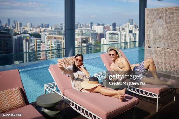 asian couple taking a selfie on sunbed at hotel pool - the weekend in news around the world stock pictures, royalty-free photos & images