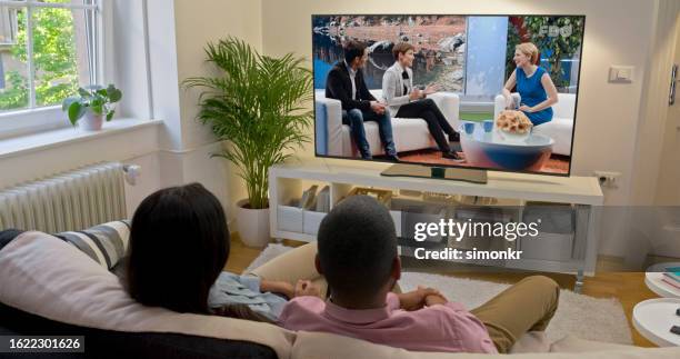 couple watching tv at home - tv stockfoto's en -beelden