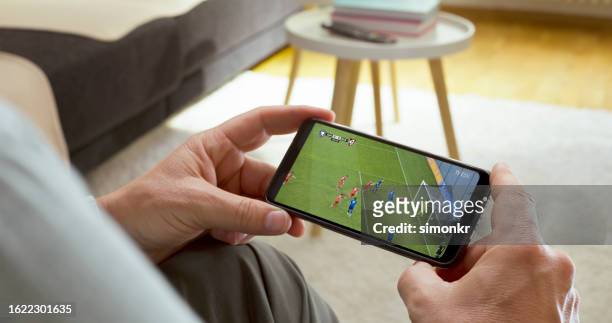uomo che guarda il calcio sul telefono intelligente - football phone foto e immagini stock