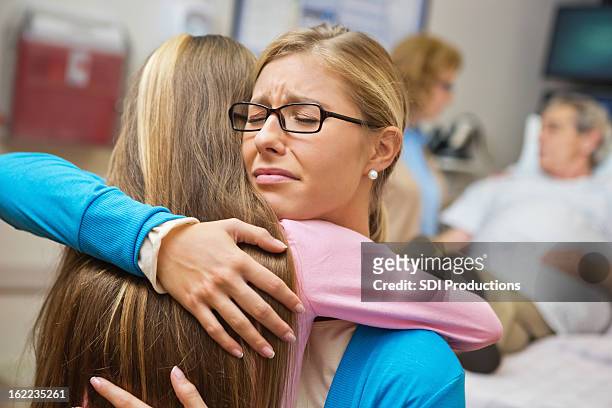 upset mom and daughter embracing in grandfather's hospital room - moms crying in bed stockfoto's en -beelden