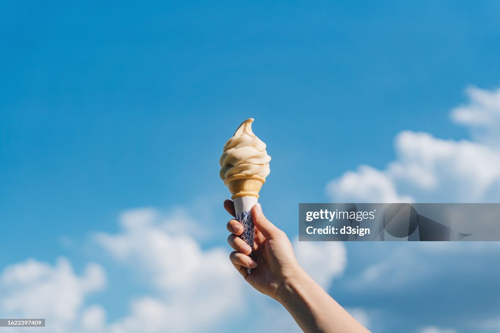 Cropped shot of woman's hand holding ice-cream cone against beautiful blue sky. It's summer! Beach holiday and vacation concept