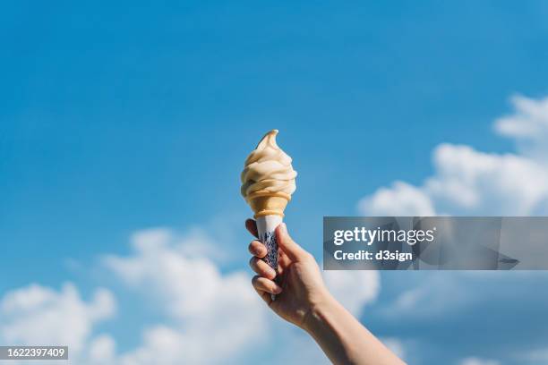 cropped shot of woman's hand holding ice-cream cone against beautiful blue sky. it's summer! beach holiday and vacation concept - glasstrut bildbanksfoton och bilder