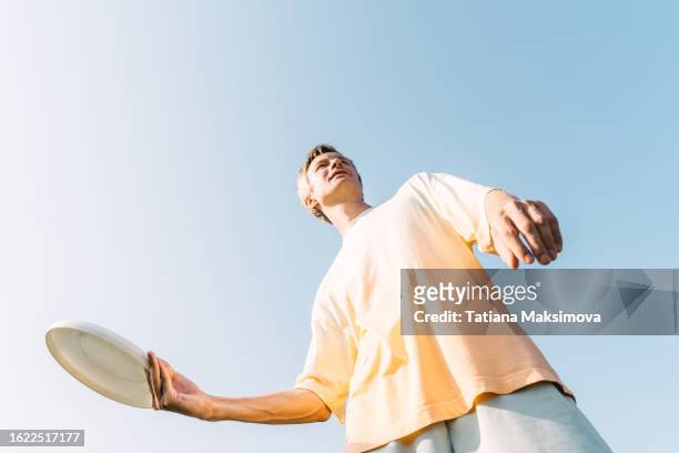 young man with flying disc frisbee in hands, bottom view, blue sky background. concept of sport in summer. - frisbee golf stock pictures, royalty-free photos & images