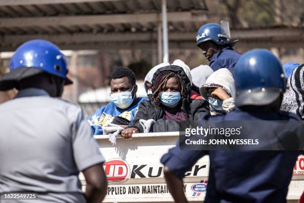 Zimbabwe Republic Police officers stand guard as some three dozen local election observers sit in a flat bed truck ahead of their court hearing at...