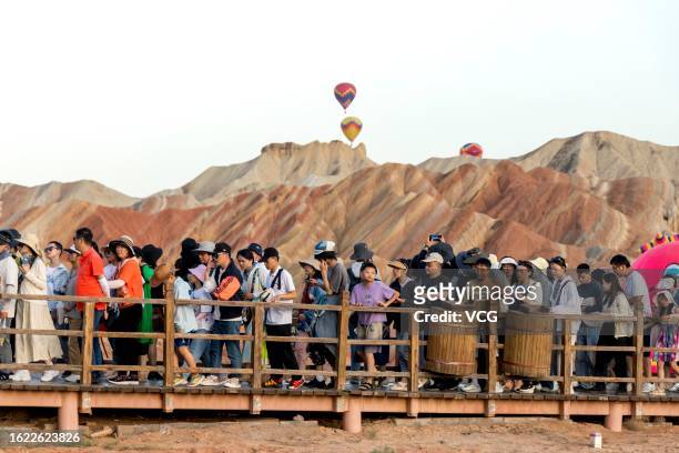 Visitors look at hot air balloons flying over Danxia landform during the third Zhangye Colorful Danxia Hot Air Balloon Festival at the Zhangye...