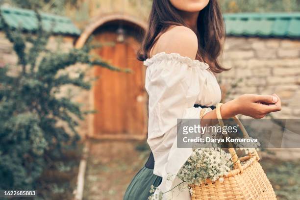 a fairy-tale unrecognisable woman is standing near her house in the forest, a woman in a costume with a basket with flowers in her hands is looking away. medieval costume for your story. book cover design with a copy space. - romance book covers stock pictures, royalty-free photos & images