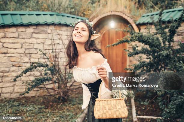 a fairy-tale elf near her house in the forest, a woman in a costume with a basket in her hands is looking away. medieval costume and elf ears for your story. book cover design with a copy space. - romance book covers stock pictures, royalty-free photos & images