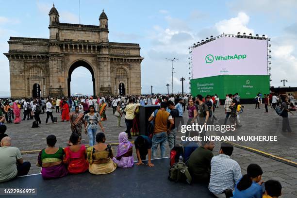 Tourists are seen at the forecourt of the iconic Gateway of India as a digital display of messaging app WhatsApp is displayed, in Mumbai on August...