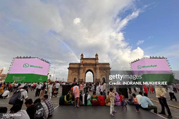 Tourists are seen at the promenade of the iconic Gateway of India next to digital displays of messaging app WhatsApp, in Mumbai on August 25, 2023.