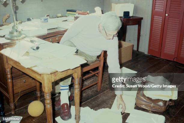 In the paper-strewn writing studio at his summer home, American writer and journalist George Plimpton works at his desk, Wainscott, New York, January...
