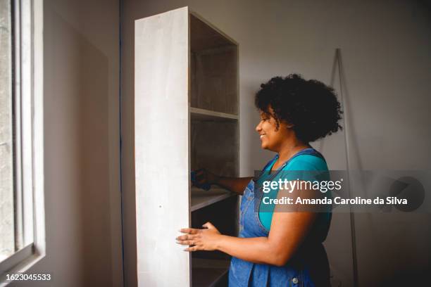 brazilian black woman painting a wooden cabinet in the middle of a renovation - reforma stock pictures, royalty-free photos & images