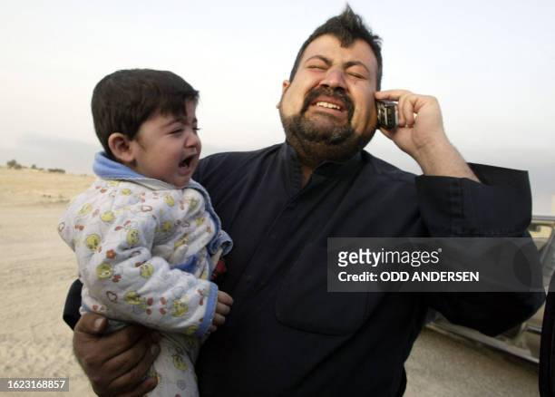 An Iragi man carrying his son cries as he speaks on a mobile phone to relatives in Kuwait after the southern Iraqi city of Safwan was overrun by...