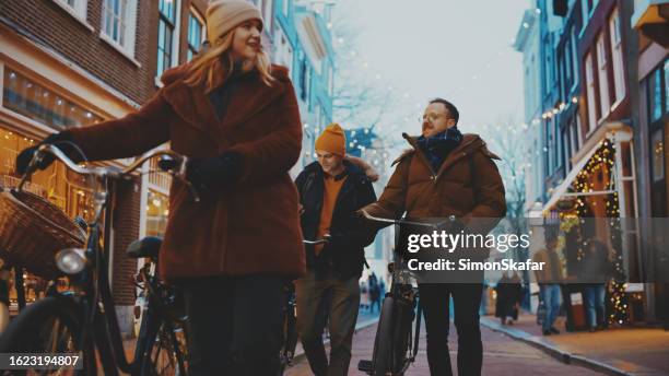 junge freunde in warmer kleidung mit fahrrädern, die auf der straße in der stadt spazieren gehen - amsterdam noel stock-fotos und bilder