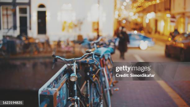 bicycles parked by railing in illuminated city of amsterdam at dusk - tyre bridge stock pictures, royalty-free photos & images