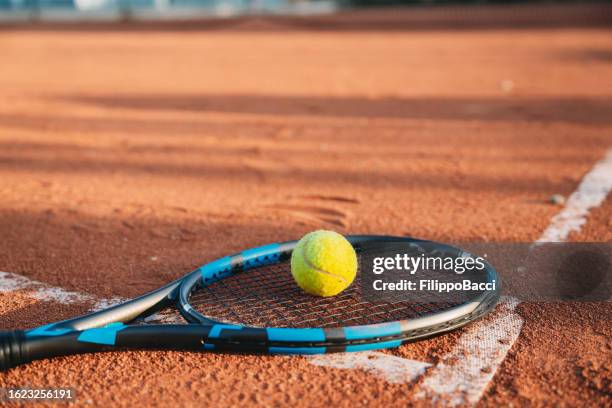 una racchetta da tennis e una palla su un campo da tennis in terra battuta - racchetta da tennis foto e immagini stock