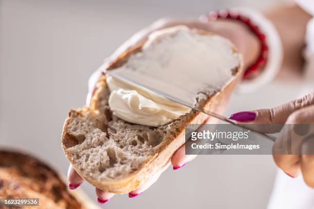 a woman makes delicious bread, spreads cream cheese with a cutlery knife - close up. - margarine photos et images de collection