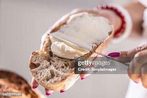 A woman makes delicious bread, spreads cream cheese with a cutlery knife - Close up. A woman makes delicious bread, spreads cream cheese with a cutlery knife - Close up.