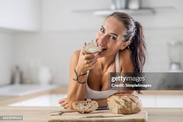 good-looking girl bites off the slice of bread with a white cheese spread. - margarine products stock pictures, royalty-free photos & images