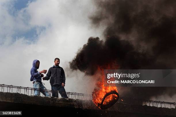 Palestinian youths push a burning tire from the roof of a concrete construction in the Shuafat refugee camp, north of Jerusalem, during the second...