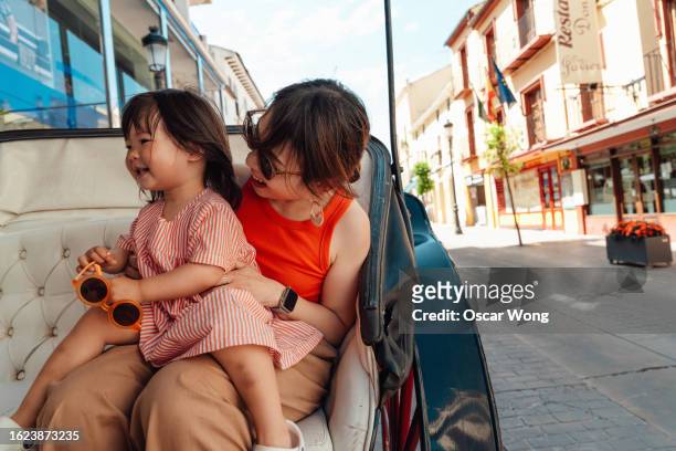 cheerful young asian mother and her little girl sitting in horse carriage on a sightseeing tour - renda stock-fotos und bilder