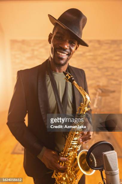 erwachsener schwarzer jazzkünstler lächelt in die kamera und hält ein saxophon - bläser stock-fotos und bilder