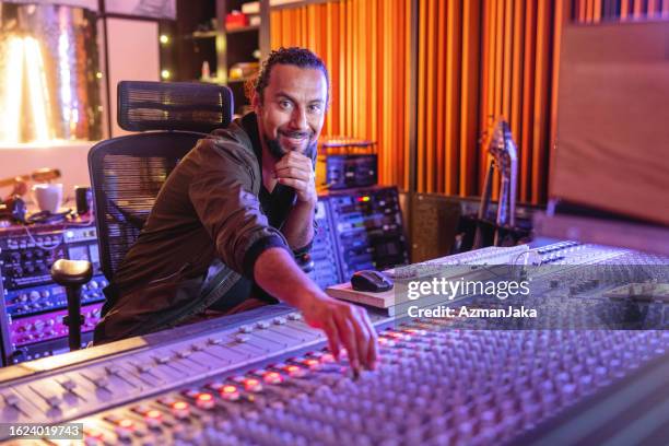 a smiling black male audio engineer readjusting the sound while looking at the camera in a recording studio - sound engineer stock pictures, royalty-free photos & images