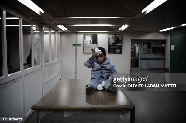 Wounded Palestinian girl holds a wad of cotton wool against her forehead as she sits on a desk at Al-Shifa hospital in Gaza City on January 21, 2009....