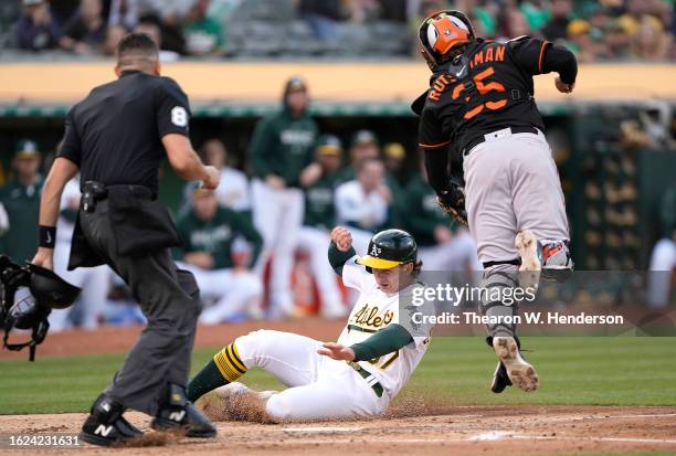 Tyler Soderstrom of the Oakland Athletics scores sliding under the tag attempt from Adley Rutschman of the Baltimore Orioles in the bottom of the...