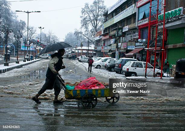 Kashmiri man holds an umbrella as he walks with his hand cart after snowfall on February 23, 2013 in Srinagar, Indian Administered Kashmir, India....